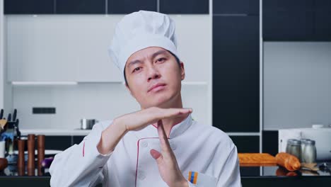 카메라를 바라보는 아시아 남성 요리사와 집 주방에 서 있는 동안 손을 움직이는 시간을 보여주는 클로즈업