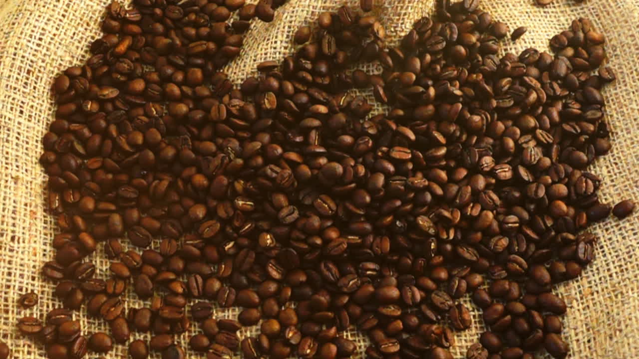Chicchi di caffè cadono su tela di iuta al rallentatore.