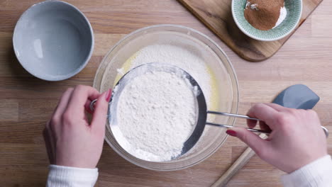 hands sifting white flour in a bowl with sieve