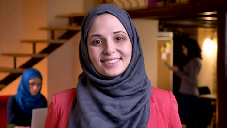 closeup portrait of young beautiful arabian female office worker looking straight at camera with cheerful smile being on the workplace indoors