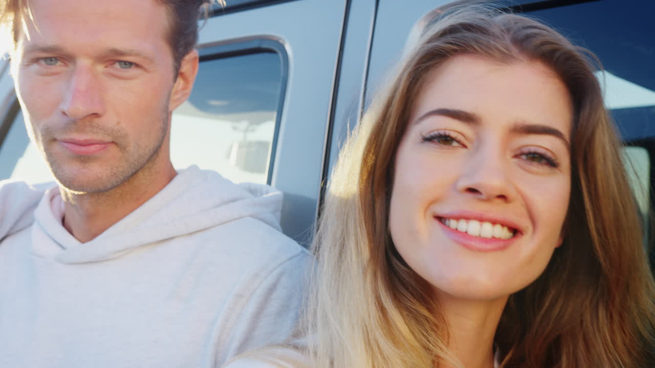 друзья в поездке стоят рядом с машиной и смотрят на камеру.