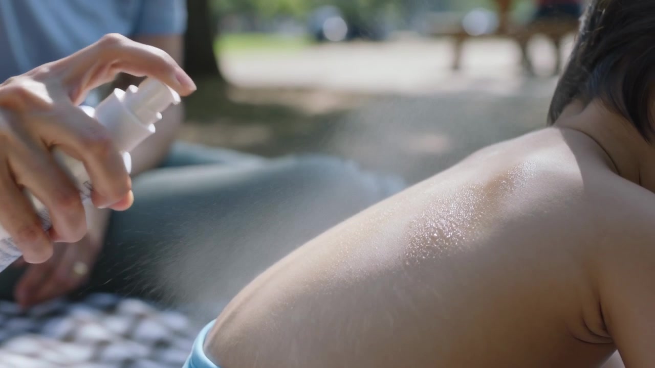 Pumping nozzle, parent spraying child's back at park for sun care with white bottle, copy space
