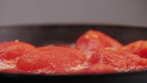 cooking fresh peeled canned tomato juice sauce in pan, peeled tomatoes boiling in their own juice, making tomatoes pasta sauce .top view close up, italian traditional cuisine food.