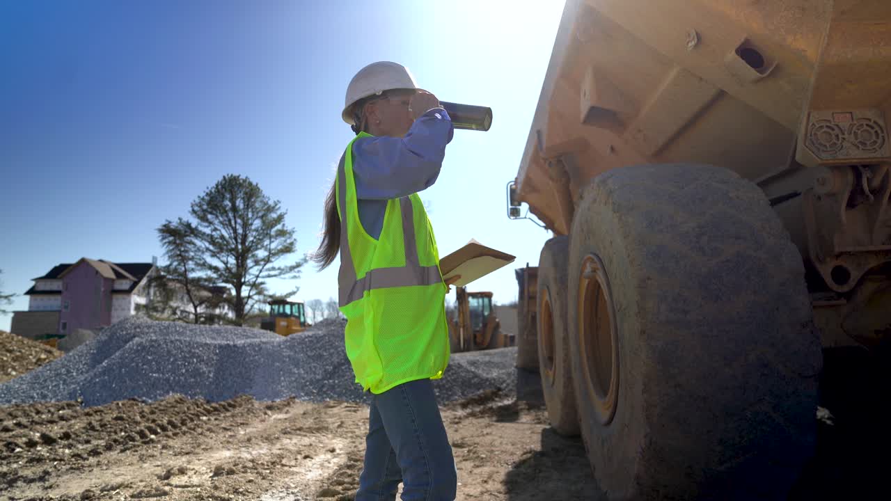 tomada desde el suelo, una vista de primer plano de una arquitecta, ingeniera, directora de proyecto con un chaleco amarillo y un sombrero duro en un sitio de construcción bebiendo de una taza aislada