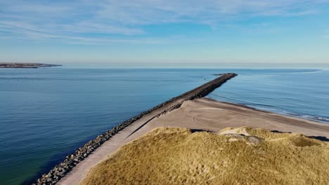a drone captures a cement block water breaker extending into the north sea from a sandy beach in western denmark.
