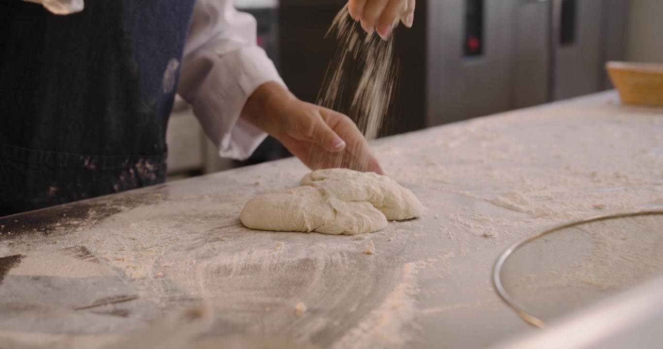 Donne fornaie di diverse etnie che premono, impastano e piegano l'impasto su un bancone infarinato, formando pagnotte per la cottura.