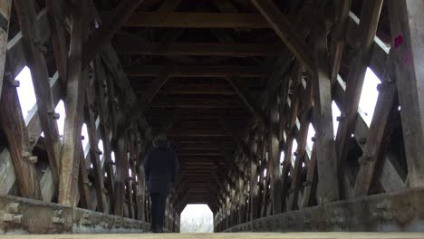 Low-wide-angle-on-a-historic-wooden-covered-bridge-as-pedestrian-walks-through