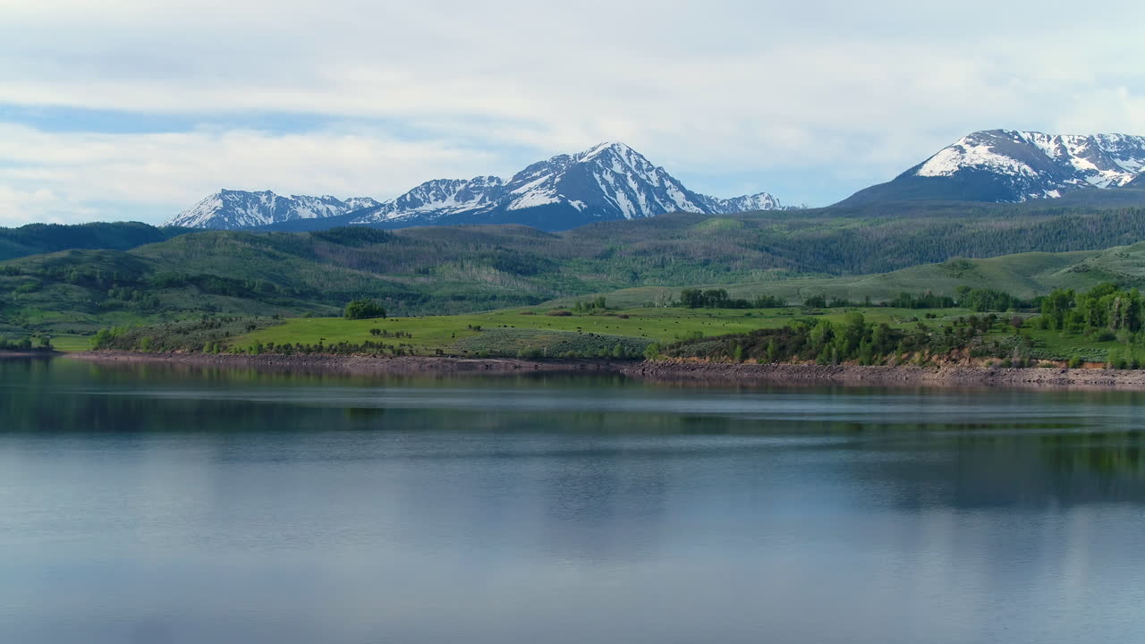 drone aéreo del lago en las montañas rocosas de colorado con árboles forestales y picos nevados en la distancia