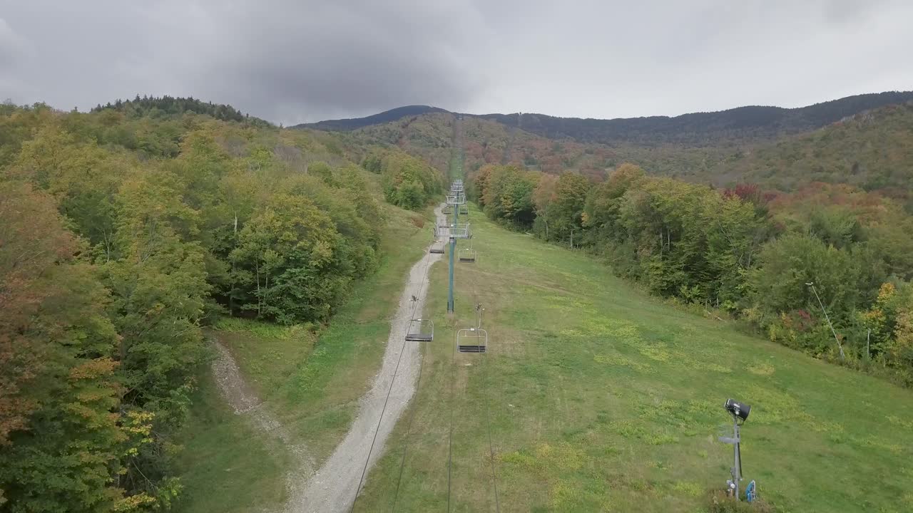 Droneflyvning, der stiger op ad en skiløjpe om efteråret, hvor løvet begynder at bryde frem, efter en stolelift op ad bjerget.