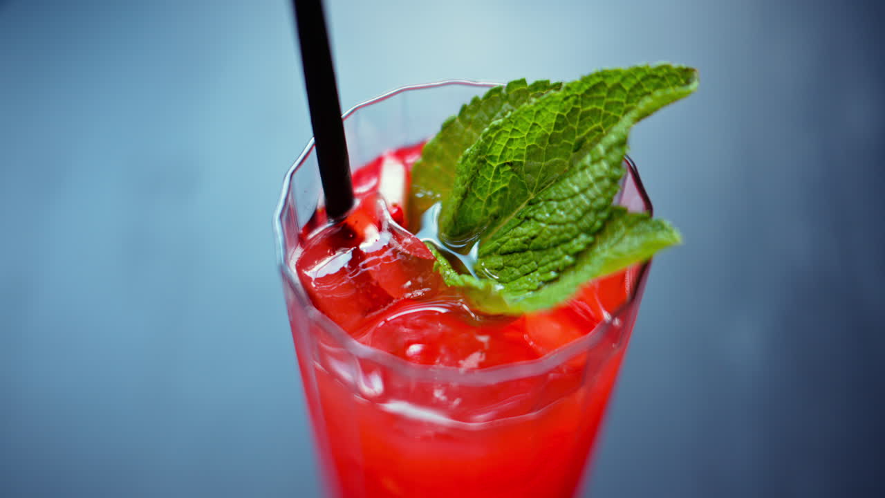 A red drink with ice and mint in a transparent glass, on a blue background