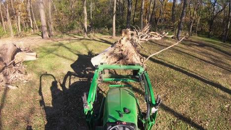 high angle point of view on small green tractor while using lift forks to move a tree stump in a clearing in the woods in autumn