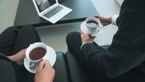 Nahaufnahme-Von-Zwei-Nicht-Erkennbaren-Geschäftsleuten,-Die-Eine-Kaffeetasse-Halten-Und-Sich-Unterhalten,-Während-Sie-Im-Büro-Auf-Dem-Sofa-Sitzen