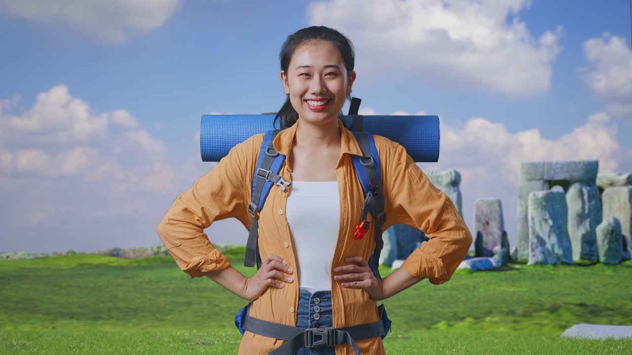 Asian Female Hiker With Mountaineering Backpack Smiling And Posing Arms Akimbo While Traveling In Stonehenge
