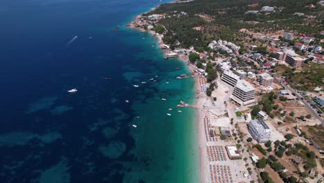 Main-beach-of-Dhermi-in-Albania,-promenade-with-cafes,-hotel,-beautiful-blue-sea-and-umbrellas