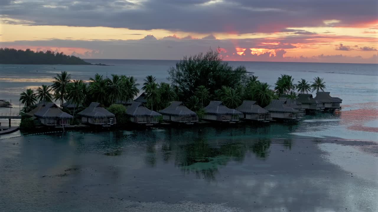 Stunning vibrant pink orange sunset sun rays Sofitel Kia Ora Resort Bungalow villas Moorea island French Polynesia aerial drone Cooks Opunohu Bay lagoon coral reef Pacific Ocean circle right parallax