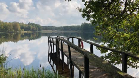 view of beautiful, calm lake surrounded by trees with wooden platform, panning shot