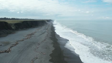 aerial reversal along stony beach as waves roll in - hakatere beach alluvial cliffs - new zealand