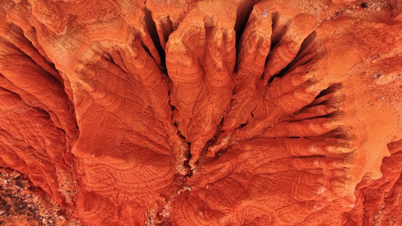 Vista dall'alto di creste di erosione a forma di ventaglio nella terra rossa, Spagna. Dita di argilla simmetriche si irradiano da un canalone centrale in calde tonalità arancioni.