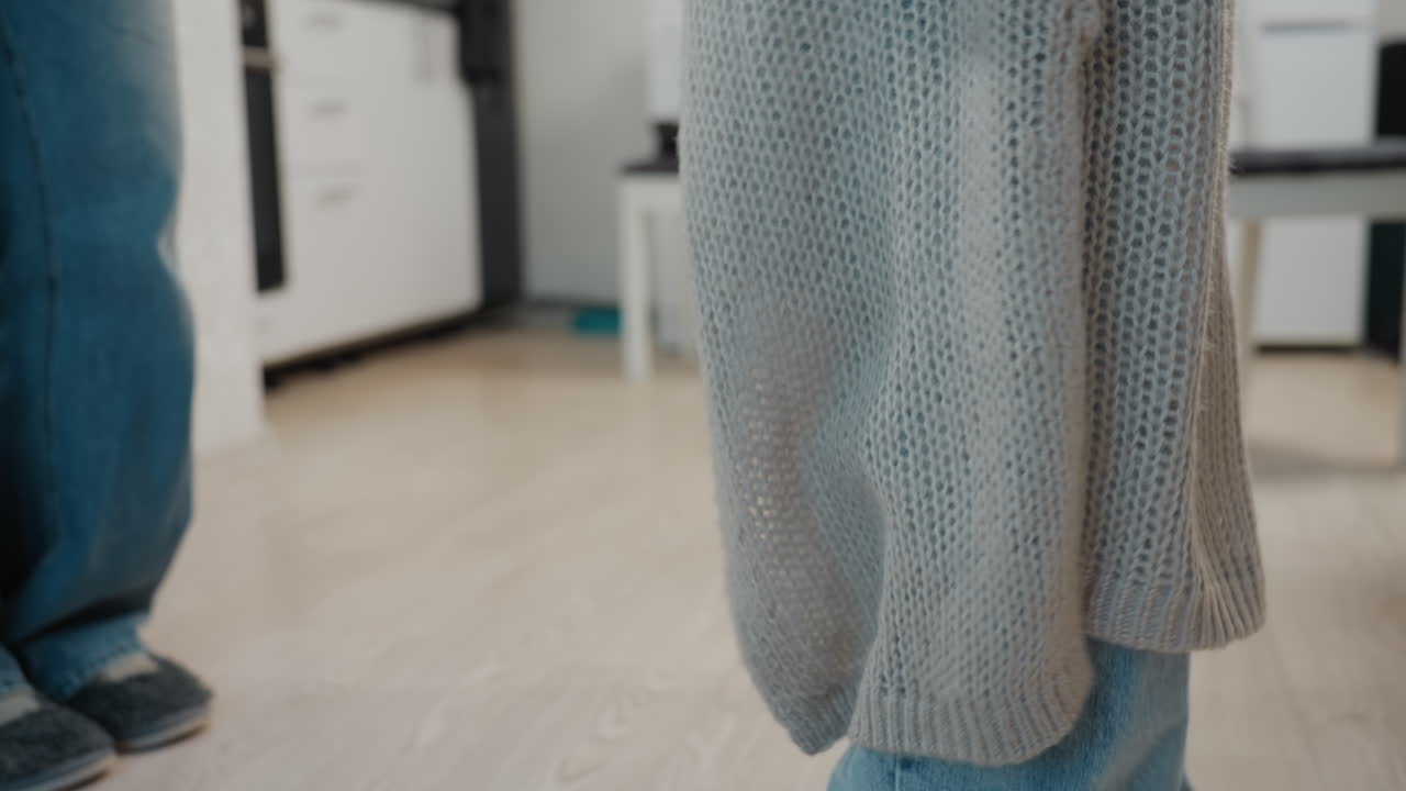 Relaxed Woman Wearing Cardigan And Jeans Inside, Casual Woman Holding Phone In Comfortable Apartment Setting, Woman In Cozy Cardigan And Jeans Standing Relaxed With Phone In Modern Living Space