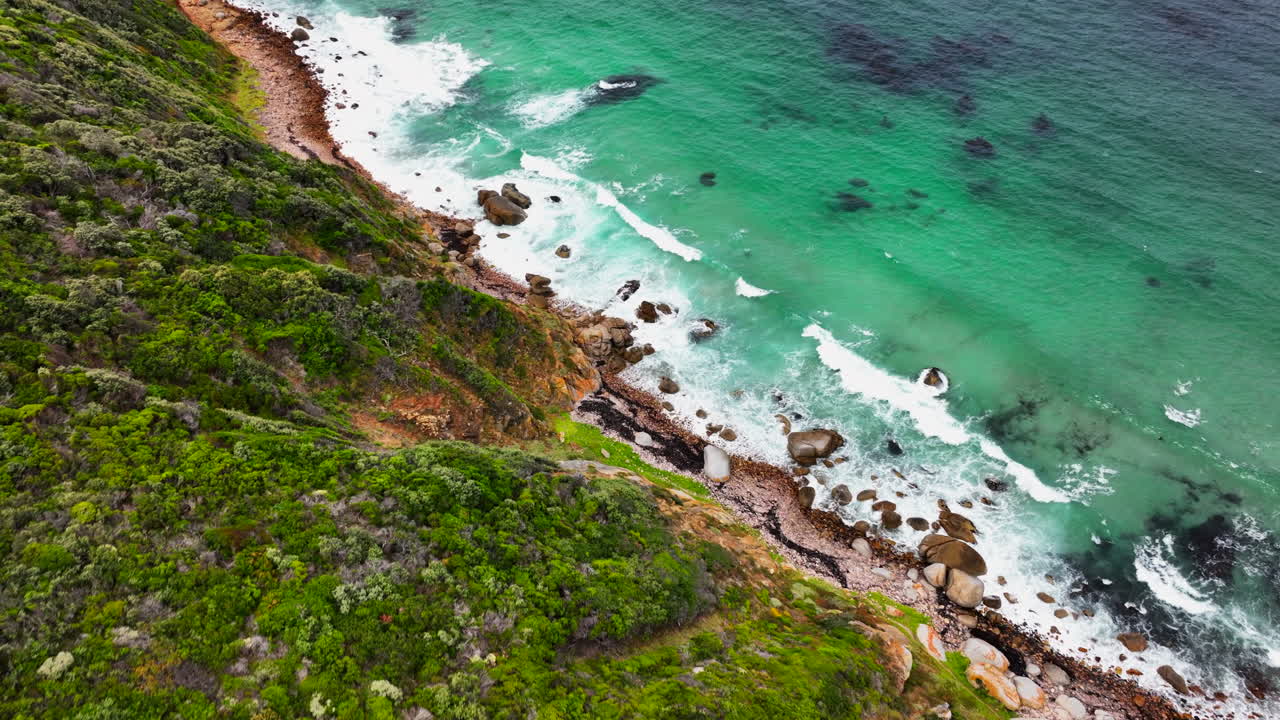 South Africa small beach town Smitswinkel Bay Cape of Good Hope Simon's Town aerial drone cinematic homes surf wave green lush spring summer deep aqua blue ocean cloudy mountain pan down movement