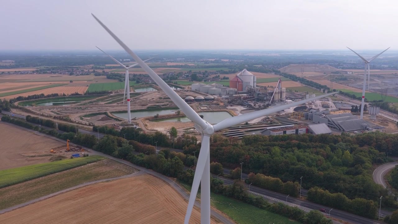 Aerial view circling a modern wind turbine with rotating blades. Sustainable energy production from a wind farm next to an industrial plant