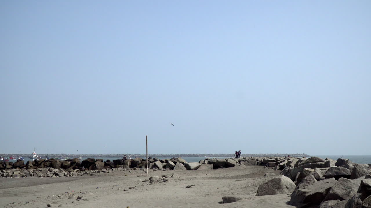 Distant view of a happy couple climbing on the rocky coastline of Playa Salverry beach, Trujillo, La Libertad, Peru