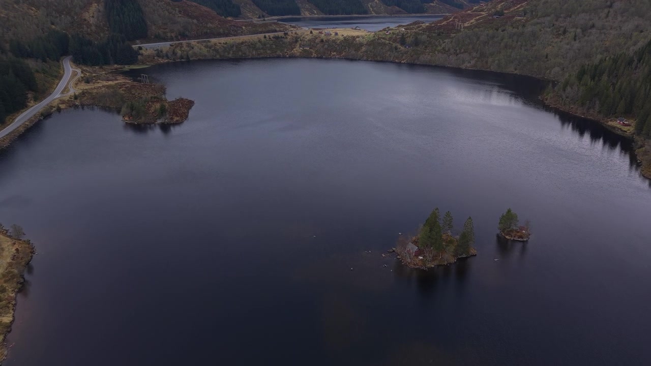 Un lago apartado con pequeñas islas rodeado de un denso bosque y una carretera sinuosa. Captura un paisaje tranquilo y remoto. Adecuado para reportajes de viajes o documentales medioambientales.