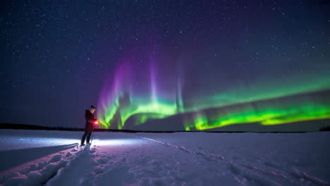 a person stands under vibrant northern lights in a snowy landscape