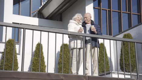 senior couple hugging while holding coffees to go on a terrace in the park on a winter day