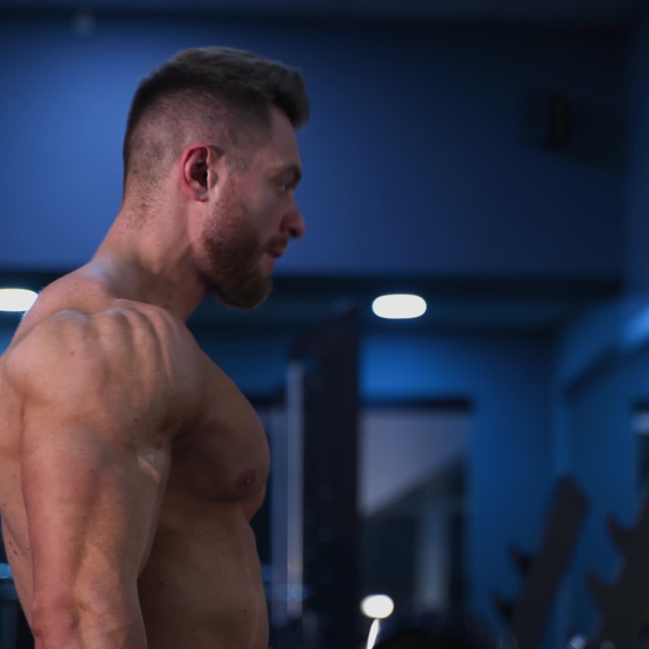 Bodybuilder forte che pompa i muscoli. Bell'atleta che si allena con i manubri. Uomo atletico che fa esercizi in palestra a torso nudo. Vista di profilo.