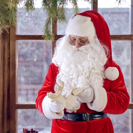 santa claus standing in specially decorated room, holding wooden dear near the new year tree. christmas spirit concept close up portrait. christmas eve. new year is coming.