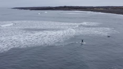 surfer balancing on surfboard while riding small wave at sandvík beach, aerial