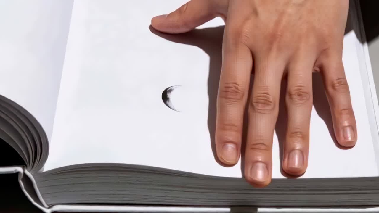 Placing adult hand holding open hardcover book at desk, keeping pages flat with crescent mark