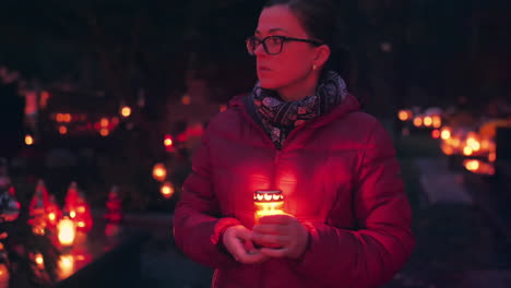 mujer visitando el cementerio por la noche sosteniendo una vela encendida