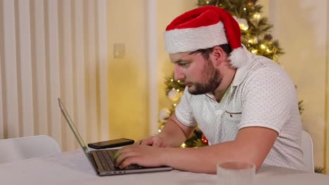 Hombre-Barbudo-Festivo-Con-Sombrero-De-Santa-Navegando-Por-Internet-En-Una-Computadora-Portátil-En-Casa-En-Navidad,-Vista-Lateral