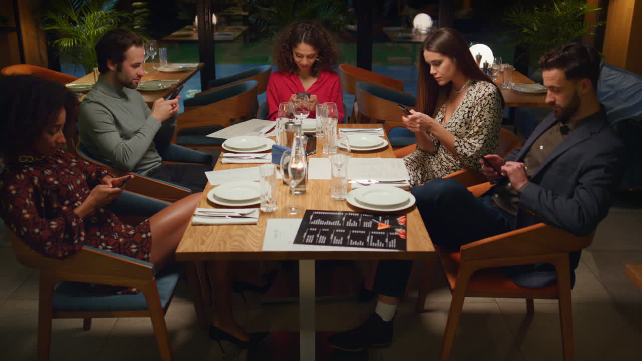 Friends table reading mobile phone browsing internet social media in restaurant.