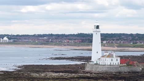 a steady side-to-side camera pan reveals st mary’s lighthouse on a rocky tidal shore under overcast daylight, with distant coastal town in background