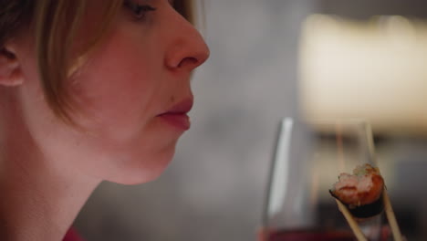 close up of girl licking sushi sauce with tongue as she eats sushi using chopstick while holding glass of red wine showing expression of enjoyment and focus in cozy indoor setting