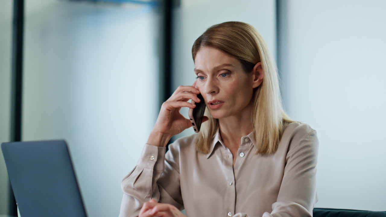 Nærbilde av en rolig direktør som snakker i smarttelefon på kontoret. Seriøs dame ringer.
