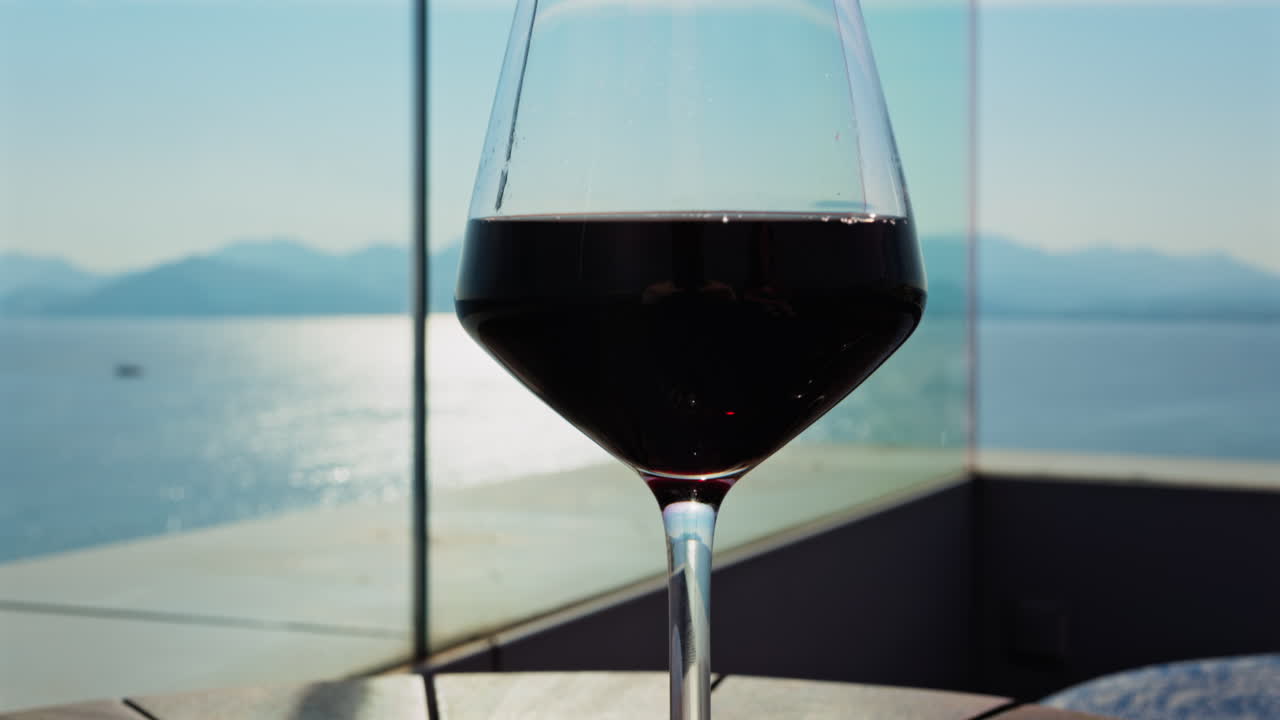 Close up of a glass of red wine and snacks on a table at a terrace with a sea view