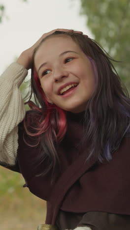 young female warrior sits holding trophy pendant from defeated enemy. girl straightens hair and smiles contentedly sitting in wooden gazebo closeup on blurred background