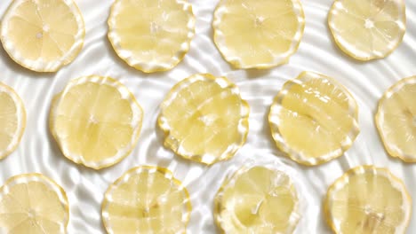 drops falls in water making rings over lemon slices on white bg