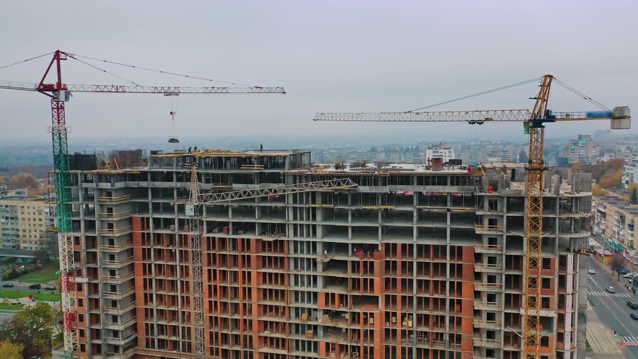 New construction in the city center. Wide high-rise building under construction outdoors. Aerial view. Camera moving around.