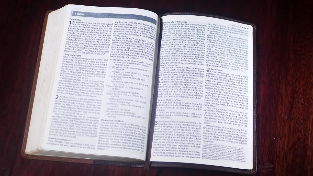 Záběr shora na Bibli v kožené vazbě otevíranou na První list Janův na dřevěném stole