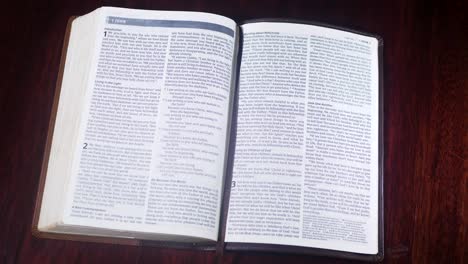 top down shot of a leather bound bible being opened up to the book of first john on a wooden table