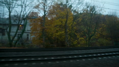 Vista-De-árboles-Otoñales-En-El-Barrio-Desde-La-Ventana-De-Un-Tren-En-Movimiento-Al-Atardecer