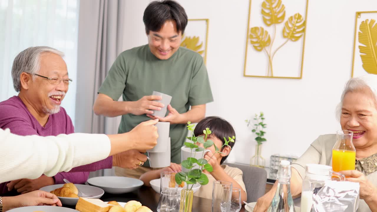 Asian family shares breakfast, pours juice, and toasts together in bright, cozy dining room