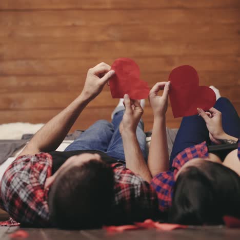 ein verliebtes paar spielt am valentinstag mit handgefertigten herzen in ihren händen auf dem bett