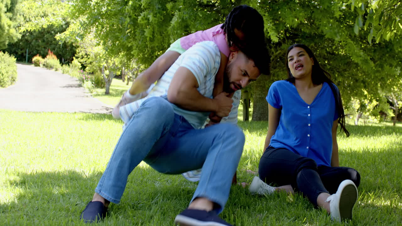 Father giving piggyback ride to child while mother laughs in sunny park