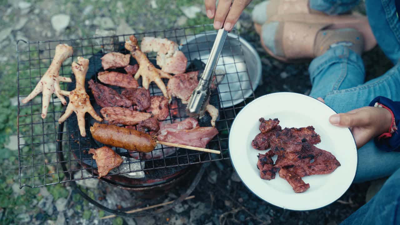 Makanan dan daging yang dipanggang di atas barbekyu di lingkungan berpenghasilan rendah di Thailand, diterangi pada malam hari, menunjukkan masakan jalanan lokal, kehidupan sehari-hari, dan budaya urban yang autentik